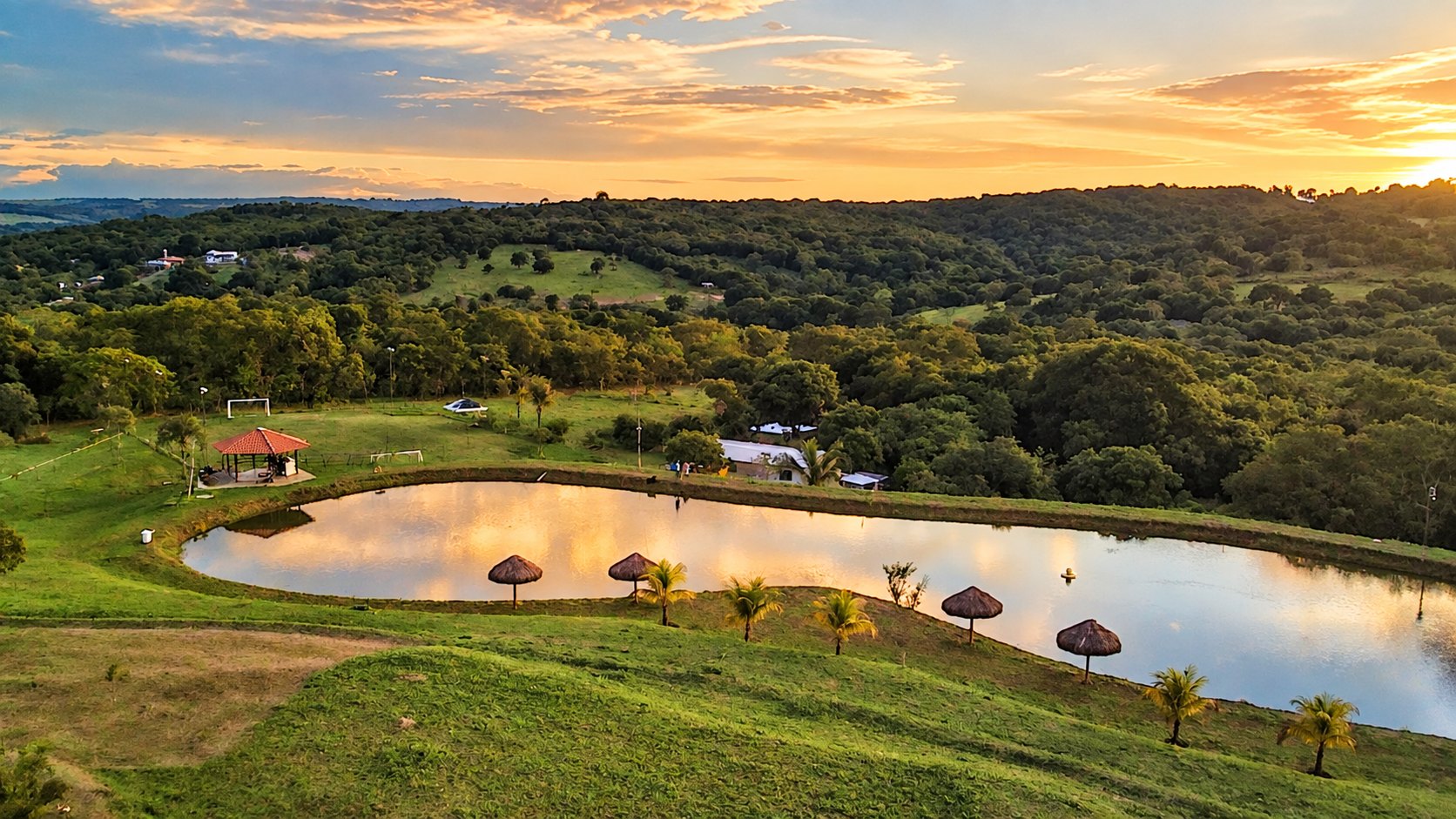 Vista aérea do Family Ranch ao pôr do sol, com lago, quiosques e mata ao redor